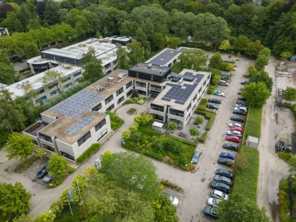 Luchtfoto van het gemeentehuis aan de Burgemeester Verderlaan met zonnepanelen op het dak en parkeerplaatsen eromheen.